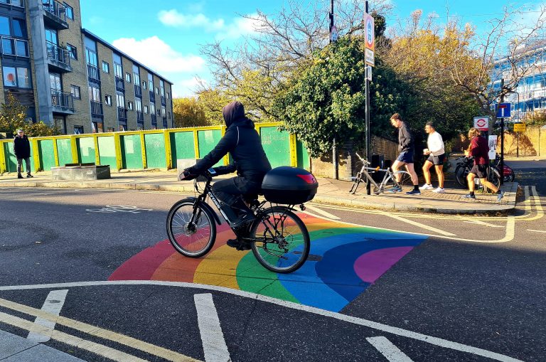 A person cycles over the rainbow on Cat and Mutton Bridge