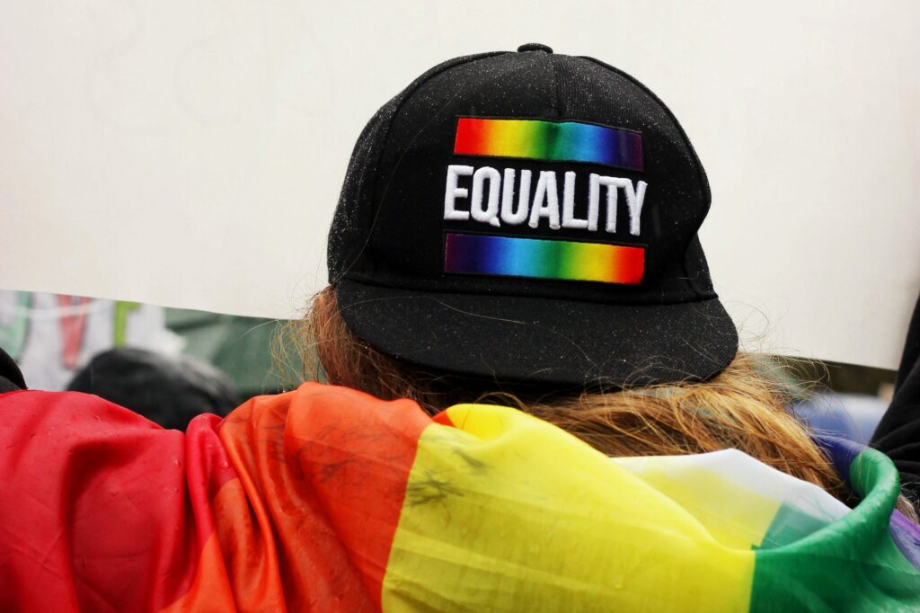 A person wrapped in a rainbow flag, wearing a hat with the word "equality" on it
