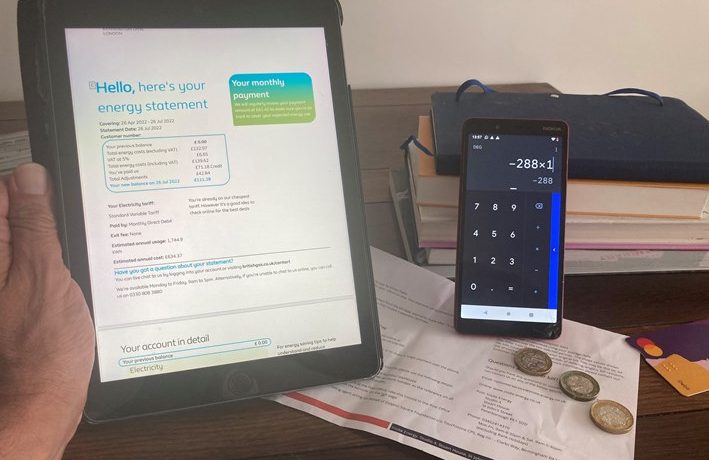 Person holding electricity bill with calculator and coins on a desk