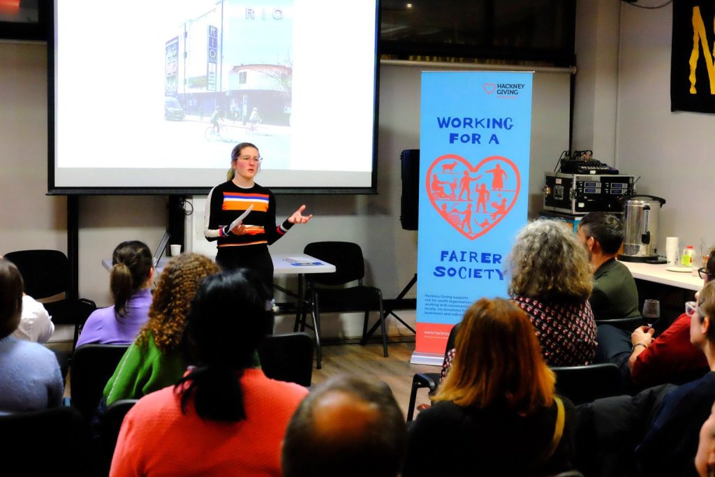 Hackney Giving programme manager presenting to an audience, next to the working for a fairer society banner